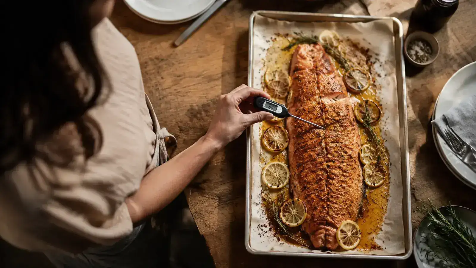 Person checking the internal temperature of a whole roasted salmon fillet on a sheet pan, thermometer probe inserted near the thickest part
