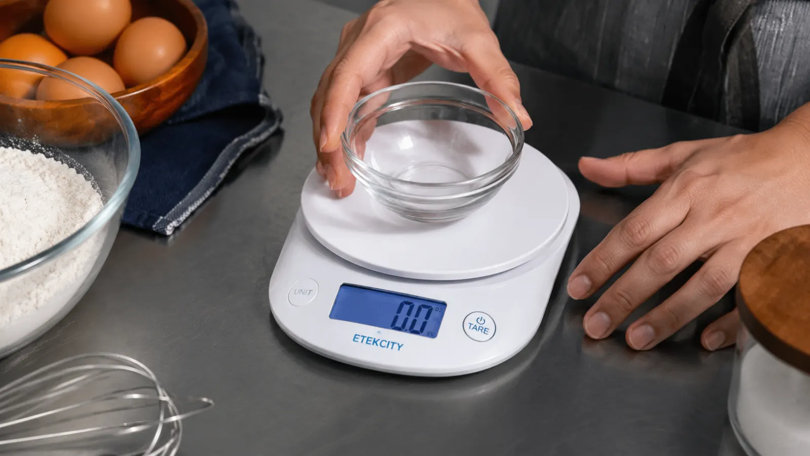 Hand placing a small glass bowl onto the Etekcity kitchen scale platform to tare before adding ingredients