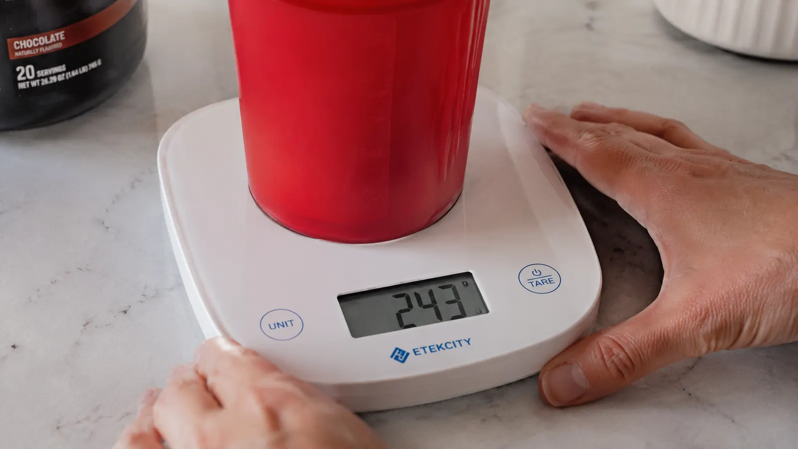 Close-up of the Etekcity scale display showing grams reading with a red protein shake cup on the platform