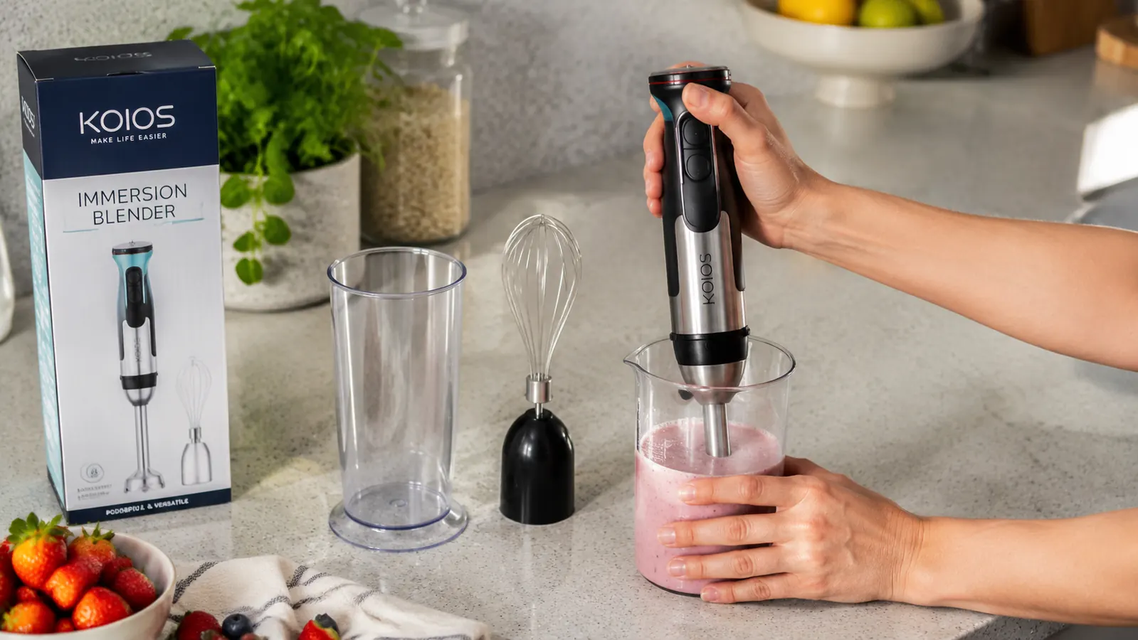 KOIOS 5-in-1 immersion blender with attachments laid out on a kitchen counter next to a glass mixing beaker