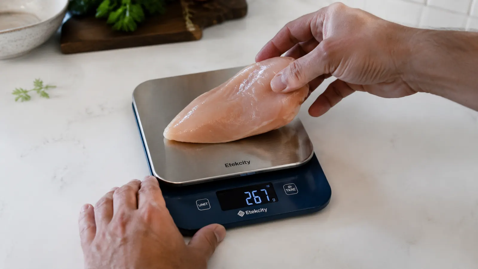 Hand placing a piece of chicken breast on the Etekcity kitchen scale platform showing grams on display