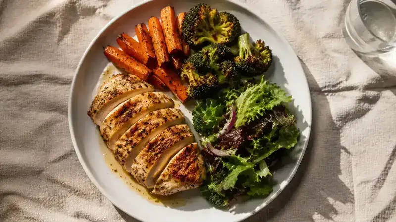 Healthy dinner plate with chicken breast, roasted vegetables, and fresh greens on a light linen placemat