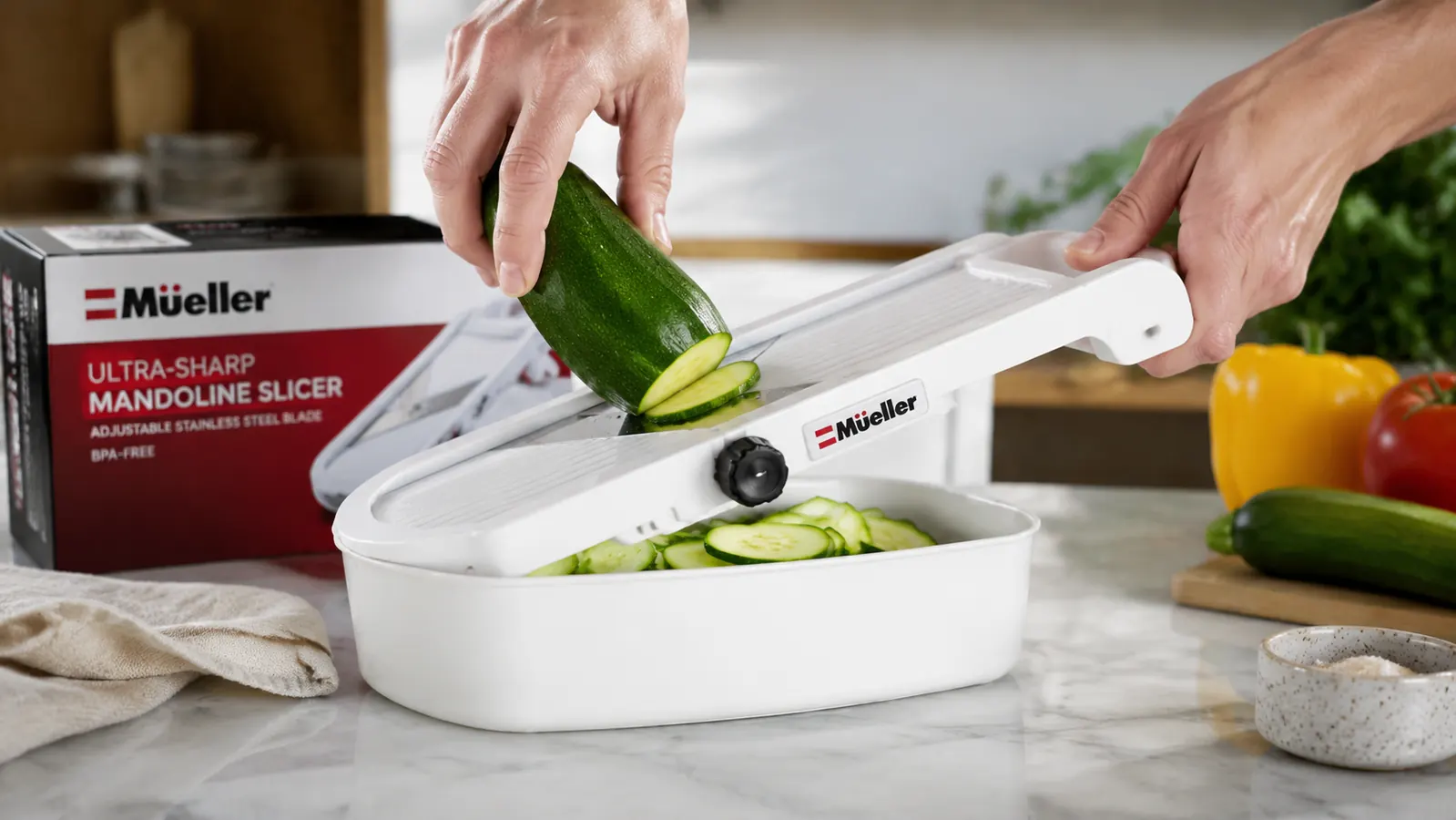 Hand sliding a zucchini across a mandoline slicer blade over a white bowl