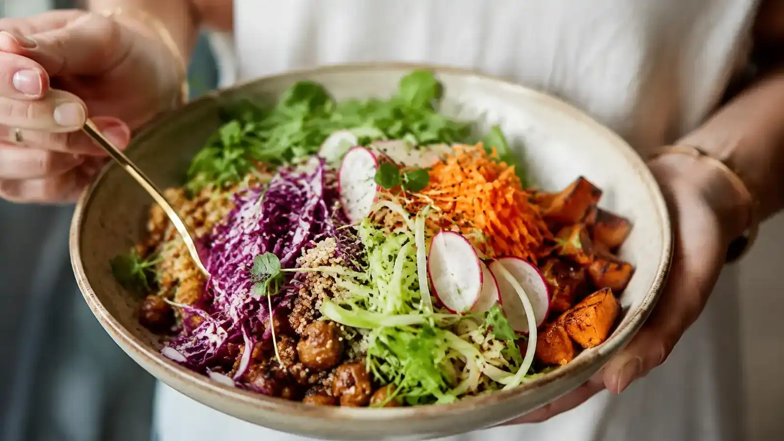 Colorful grain bowl topped with shaved radishes, julienned carrots, and paper-thin cucumber rounds