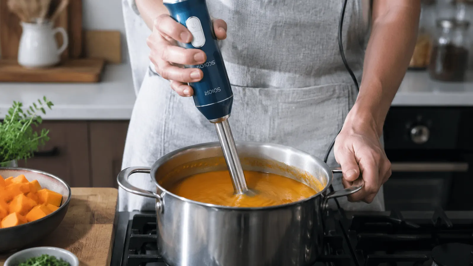 KOIOS immersion blender submerged in a pot of tomato soup, showing the blending head just below the surface