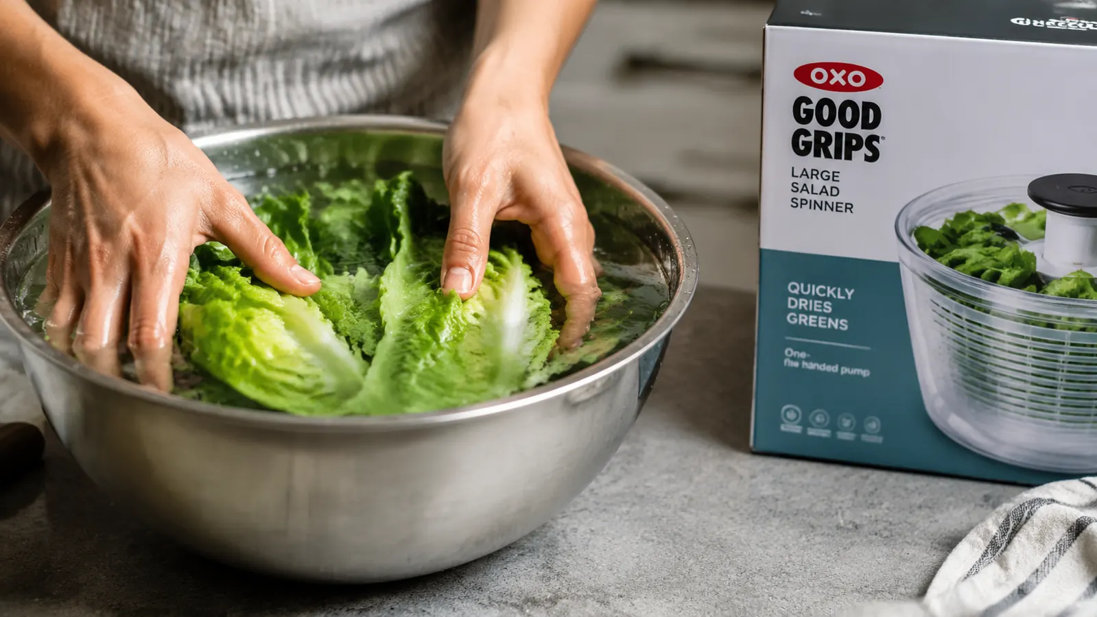 Hands submerging a bundle of green lettuce leaves in a bowl of cold water to wash them