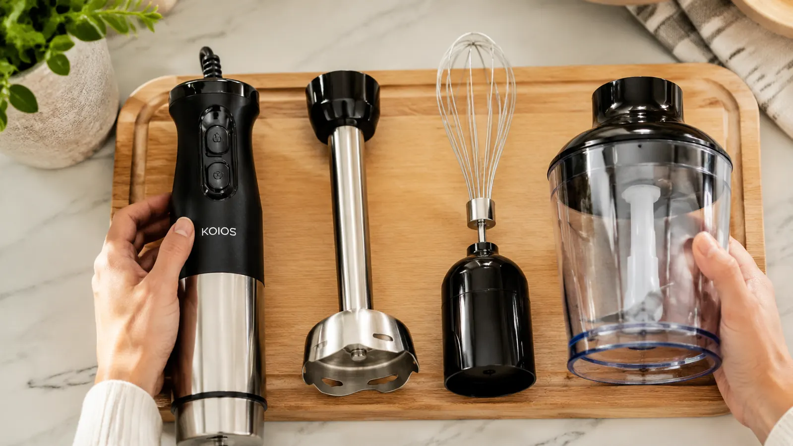 The KOIOS blender attachments laid out on a kitchen counter: blending shaft, whisk, chopper bowl, and beaker