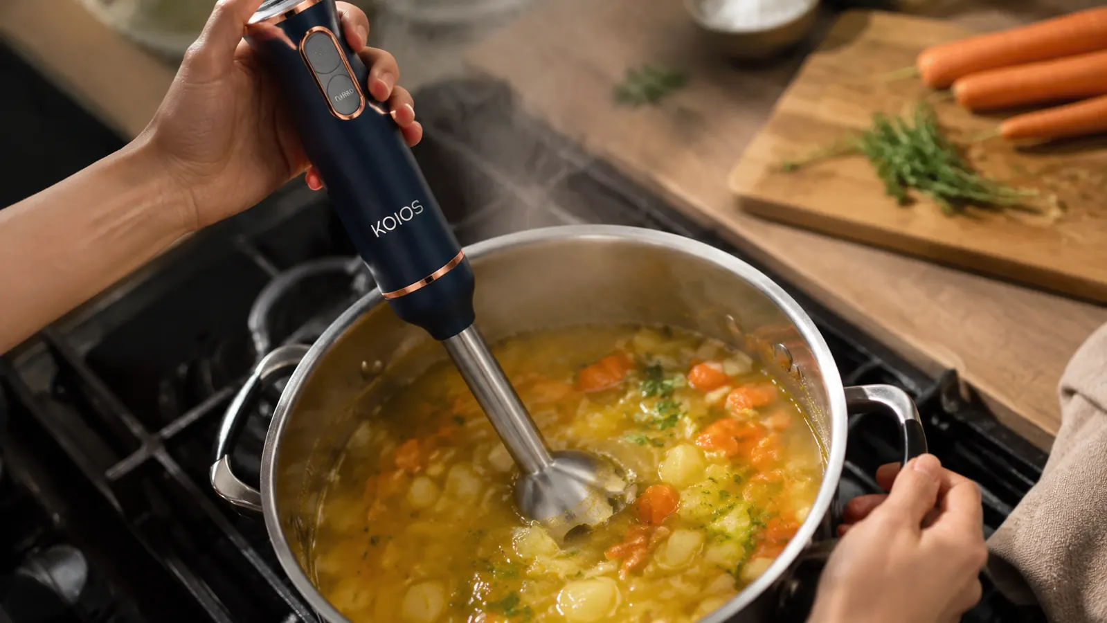 Hand holding KOIOS immersion blender submerged in a pot of vegetable soup, blending directly in the pot