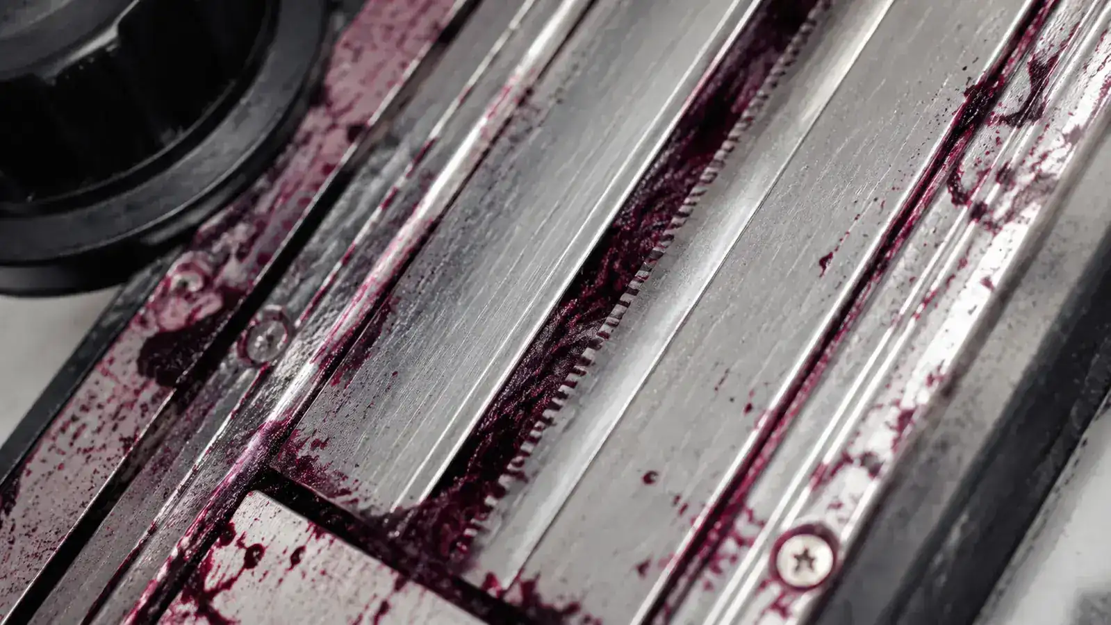 Close-up of mandoline slicer blade residue and food debris caught in the narrow blade slots after slicing beets