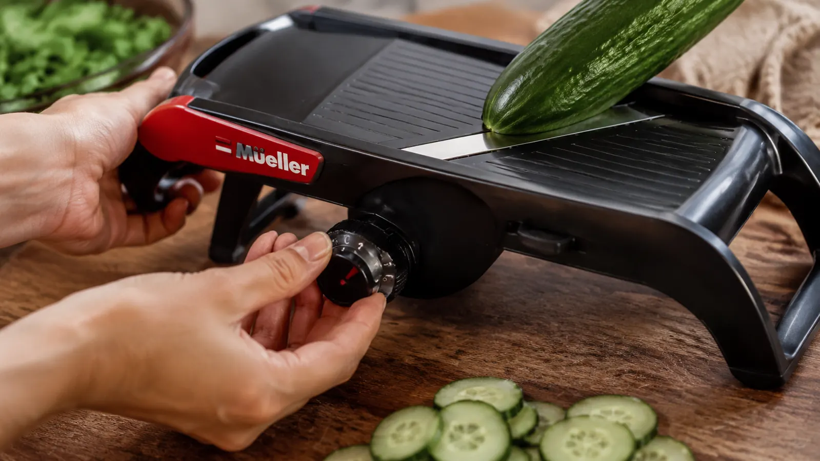 Hand adjusting the Mueller mandoline thickness dial to the 2mm setting before slicing a cucumber