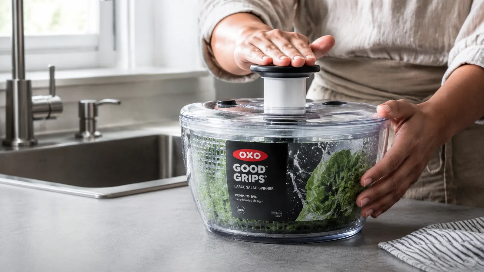 Close-up of a hand pressing the pump lid on an OXO salad spinner bowl full of wet arugula