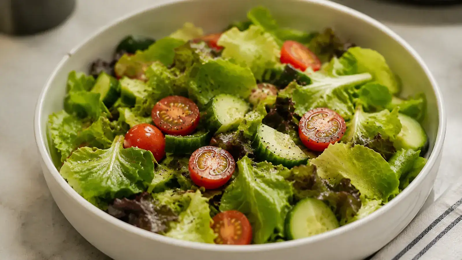 Fresh salad greens, cherry tomatoes, and sliced cucumber in a salad bowl after spinning dry
