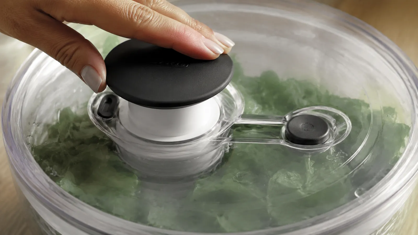 Close-up of the OXO salad spinner brake button and pump mechanism on the clear lid