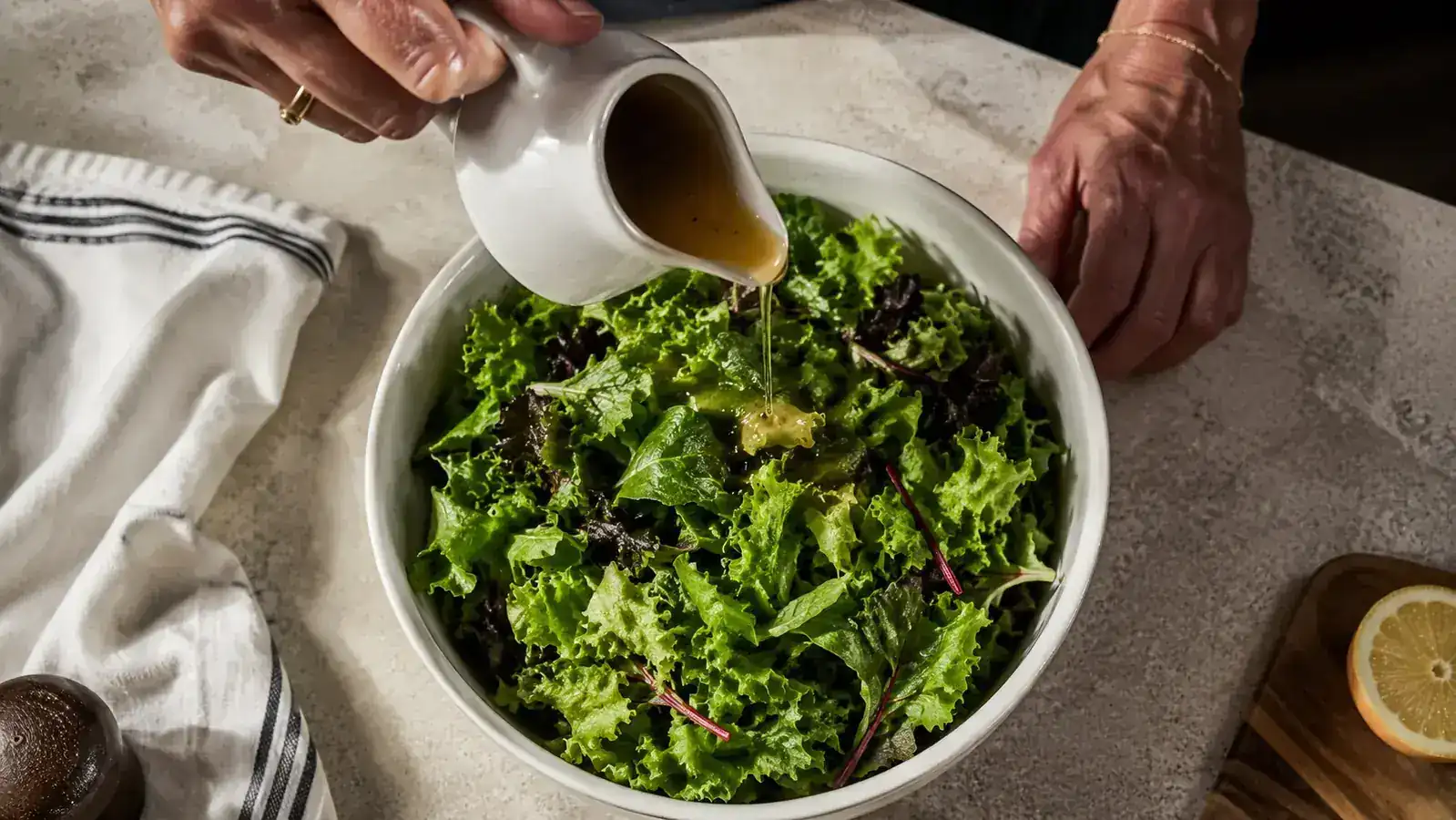 Freshly dried salad greens in a white bowl with dressing being poured over them, no water pooling at the bottom